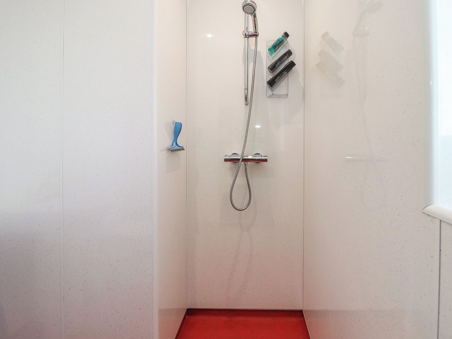 Une douche équipée d’un pommeau de douche à main, d’un robinet mural et d’un distributeur de savon.