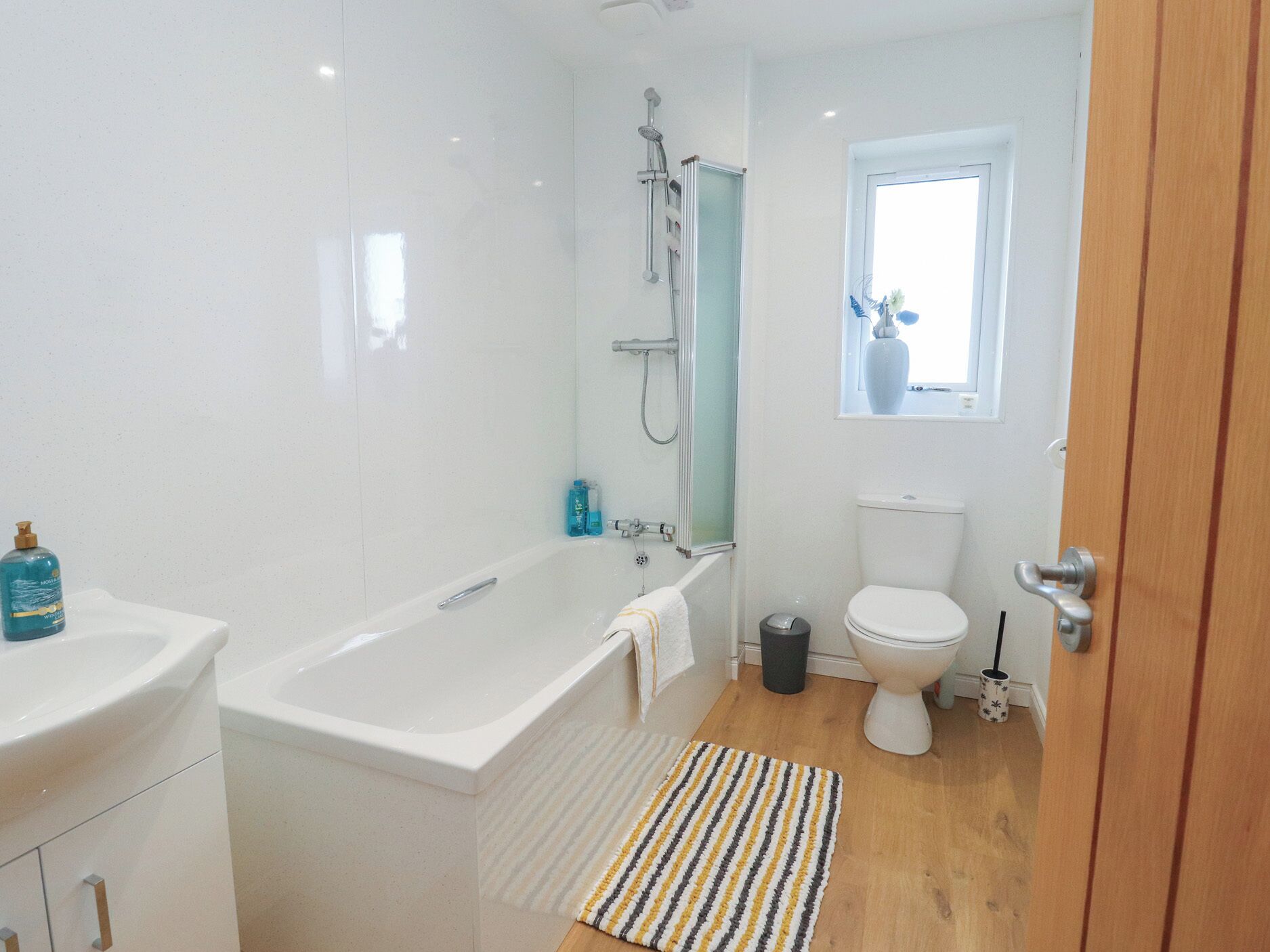 A modern bathroom with a bathtub, toilet, and a window above the toilet.