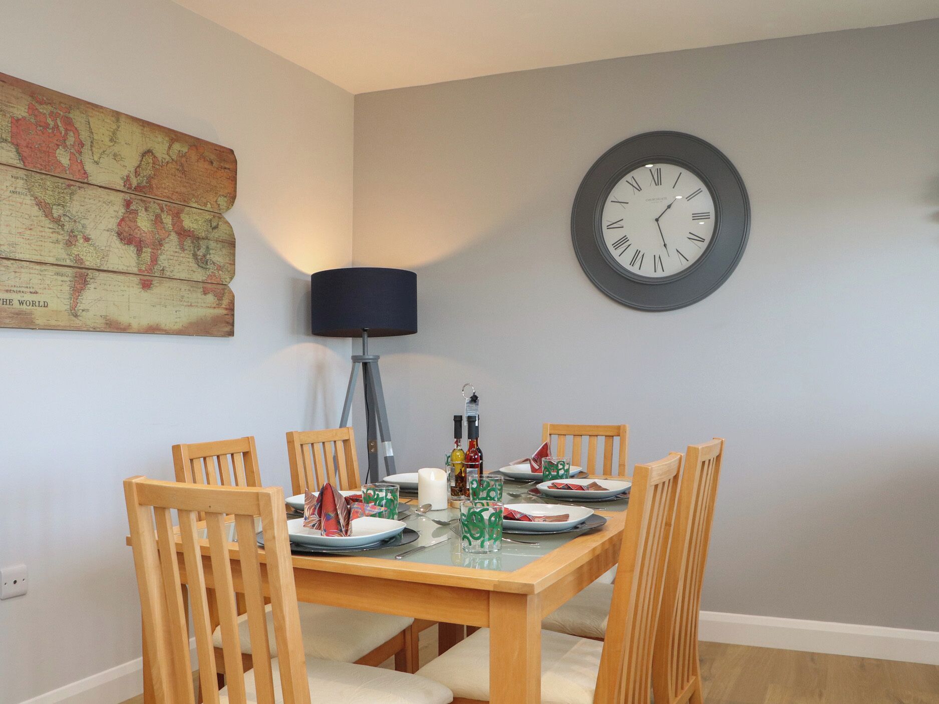 Ein Essbereich mit einem Holztisch, gedeckt für vier Personen, einer Weltkarte an der Wand, einer Uhr und einer Stehlampe.