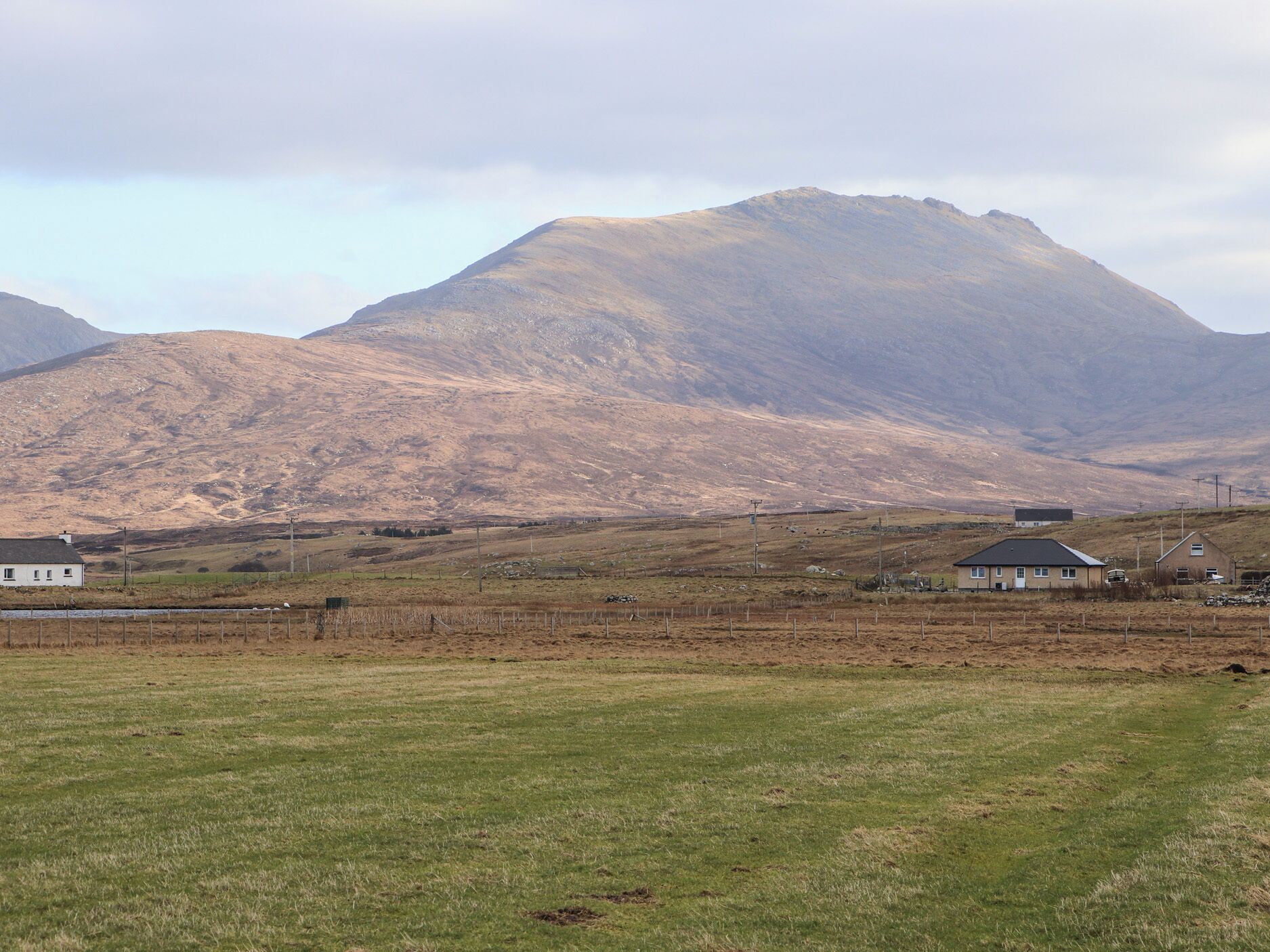 A rural landscape with a mountain in the background, a grassy field in the foreground, and several buildings including a white house and a barn.