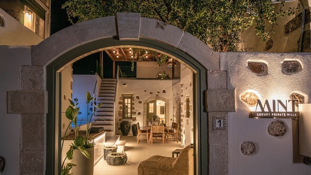 Der Eingang einer luxuriösen Privatvilla mit steinernen Bögen, einem Essbereich mit Holztischen und einem Schild mit der Aufschrift 'MINT LUXURY PRIVATE VILLA'.