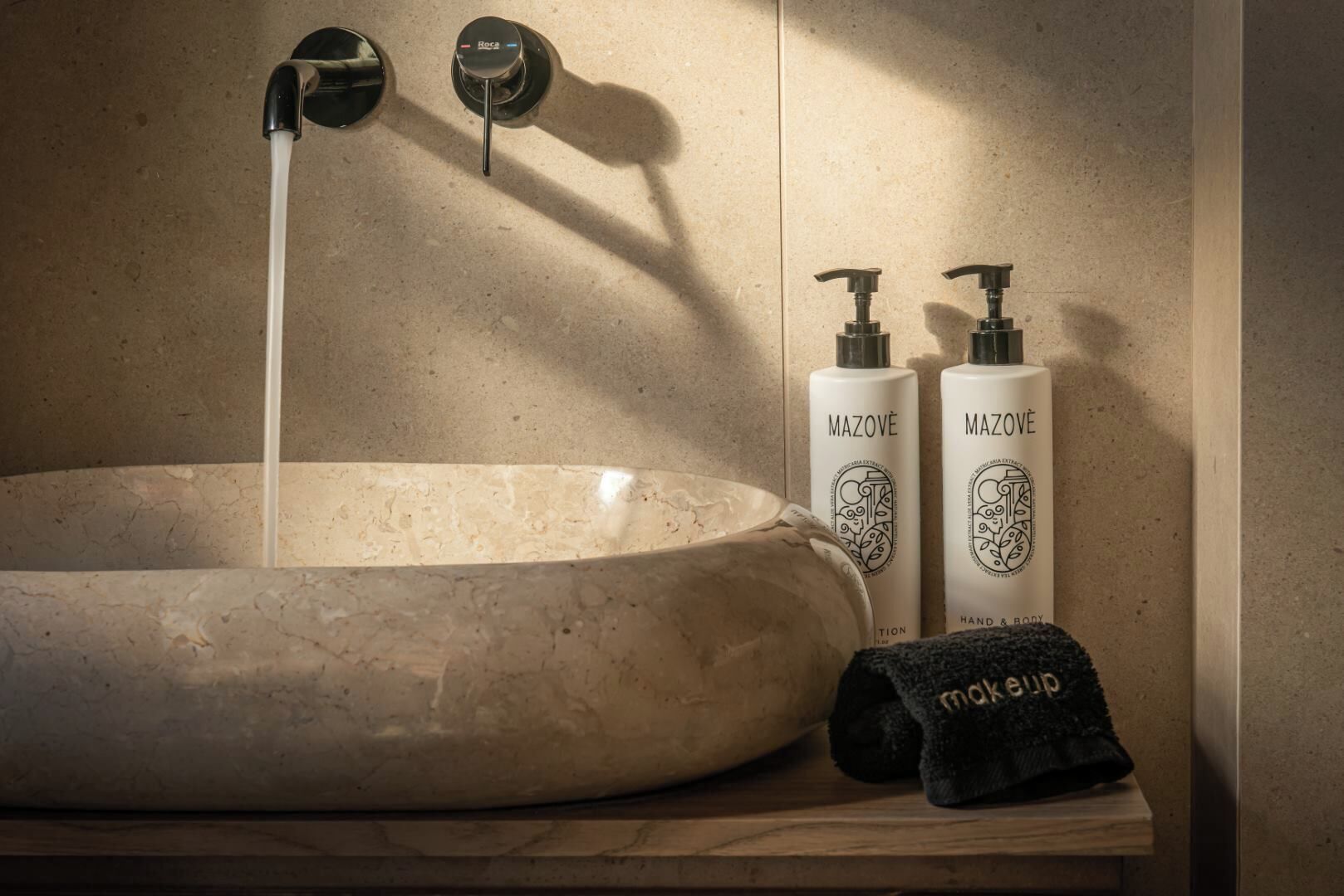 A bathroom with a large, round sink, two hand and body wash bottles, and a black towel on a wooden shelf.