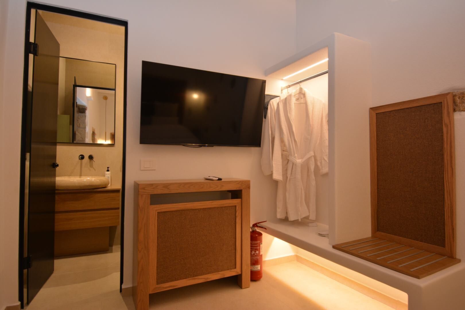 Un baño moderno con tocador de madera, televisor montado, perchero y espejo.