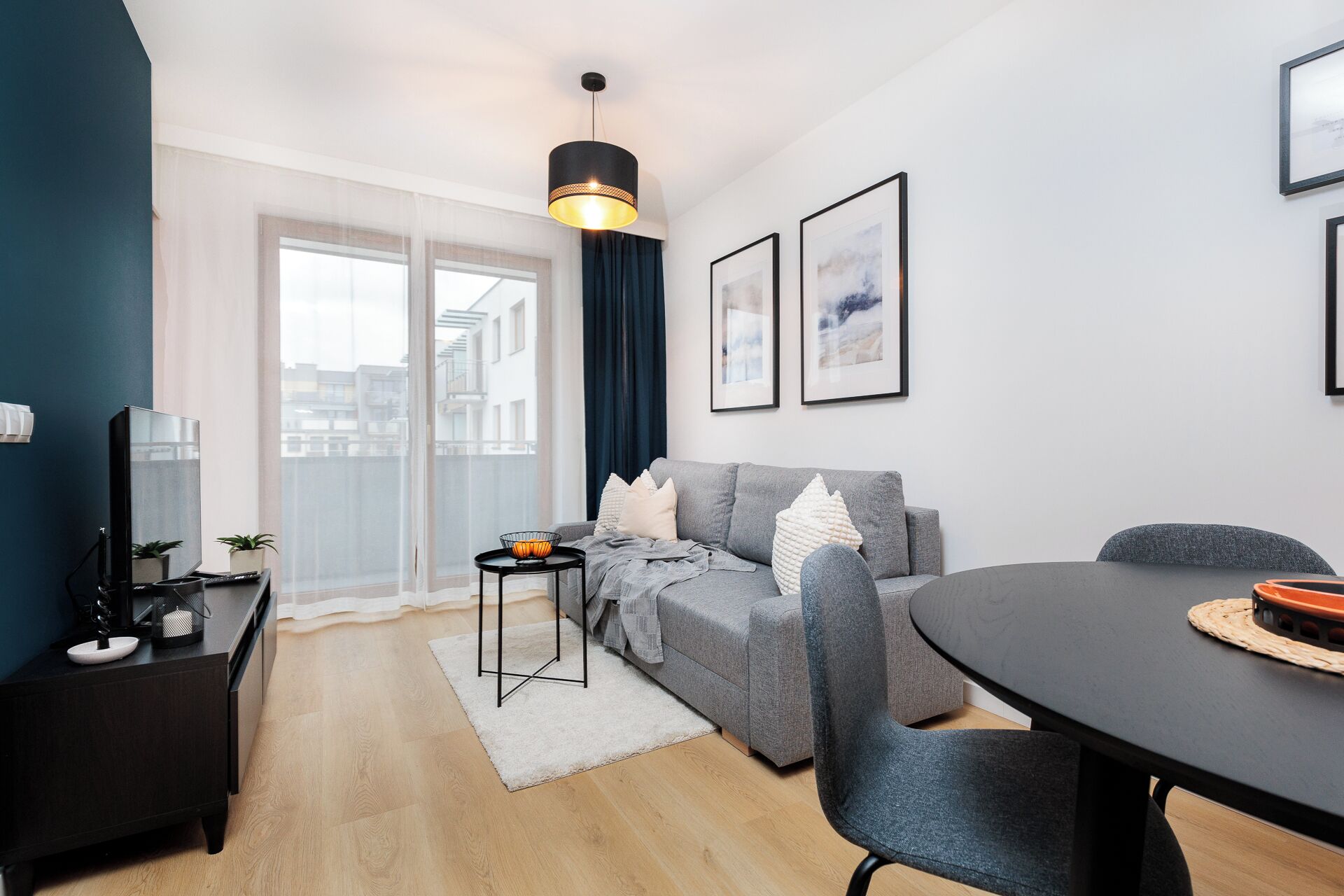 A modern living room with a grey sofa, a dining table, and a black TV stand.