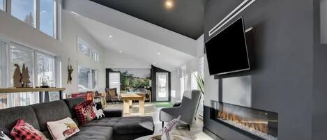 Un salon moderne doté d’une cheminée, d’un téléviseur à écran plat et d’un coin repas visible à travers une porte ouverte.