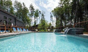A swimming pool with lounge chairs, a waterfall feature, and a building with a dark facade.