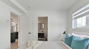 A bedroom with a bed, a nightstand, a window, and a door leading to a bathroom.