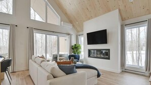 A modern living room with a white sofa, a flat-screen TV, and a fireplace. - Trinity - Familiale - Spa & Nature by Alchalet (Pont-Rouge)
