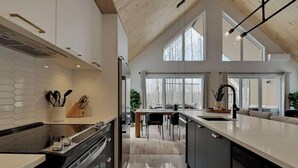 A modern kitchen with a large island, white cabinetry, and a high ceiling with exposed beams. - Trinity - Familiale - Spa & Nature by Alchalet (Pont-Rouge)