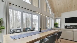 A modern interior with a long dining table, chairs, a sofa, and large windows. - Trinity - Familiale - Spa & Nature by Alchalet (Pont-Rouge)