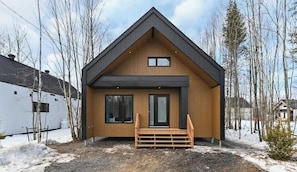 A modern house with a wooden exterior, a front porch, and a large window.