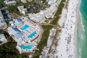 An aerial view of a resort with multiple swimming pools, a beach, and a boardwalk leading to the shore.