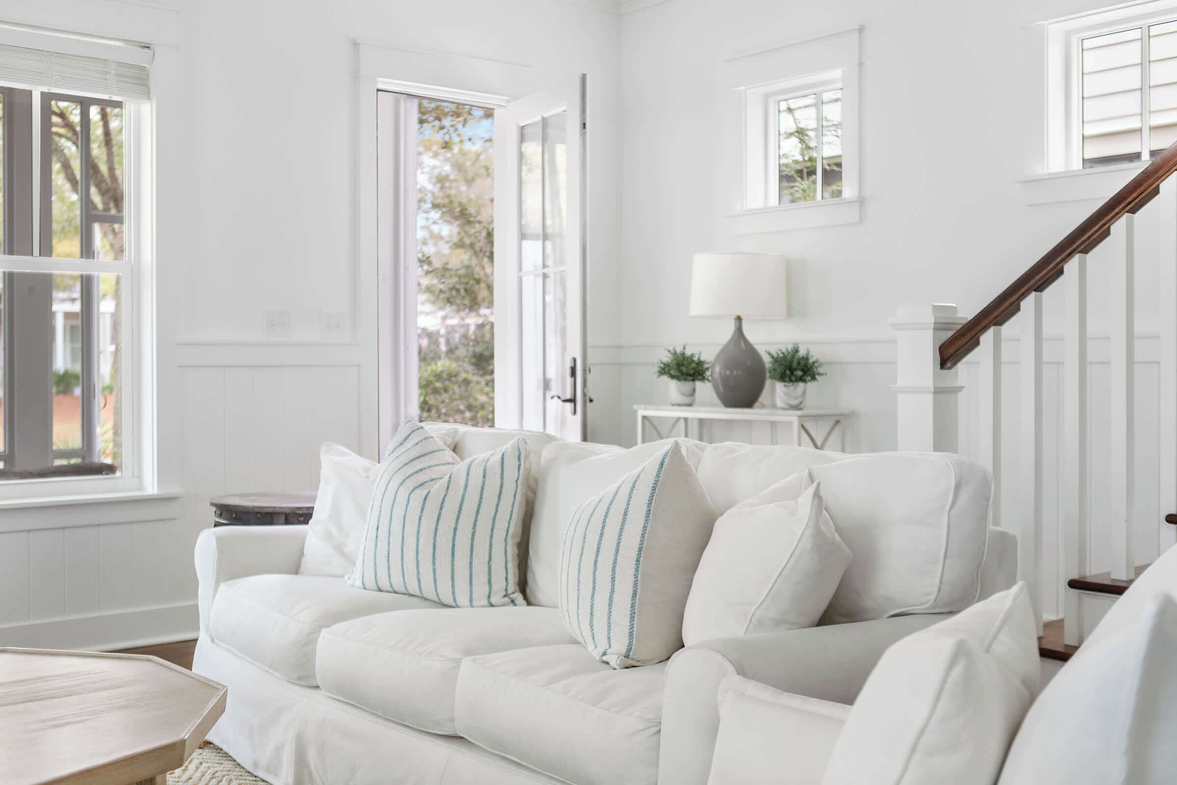 A white living room with a sofa, a lamp, and a staircase.