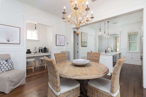 A dining area with a round wooden table, wicker chairs, and a central chandelier.