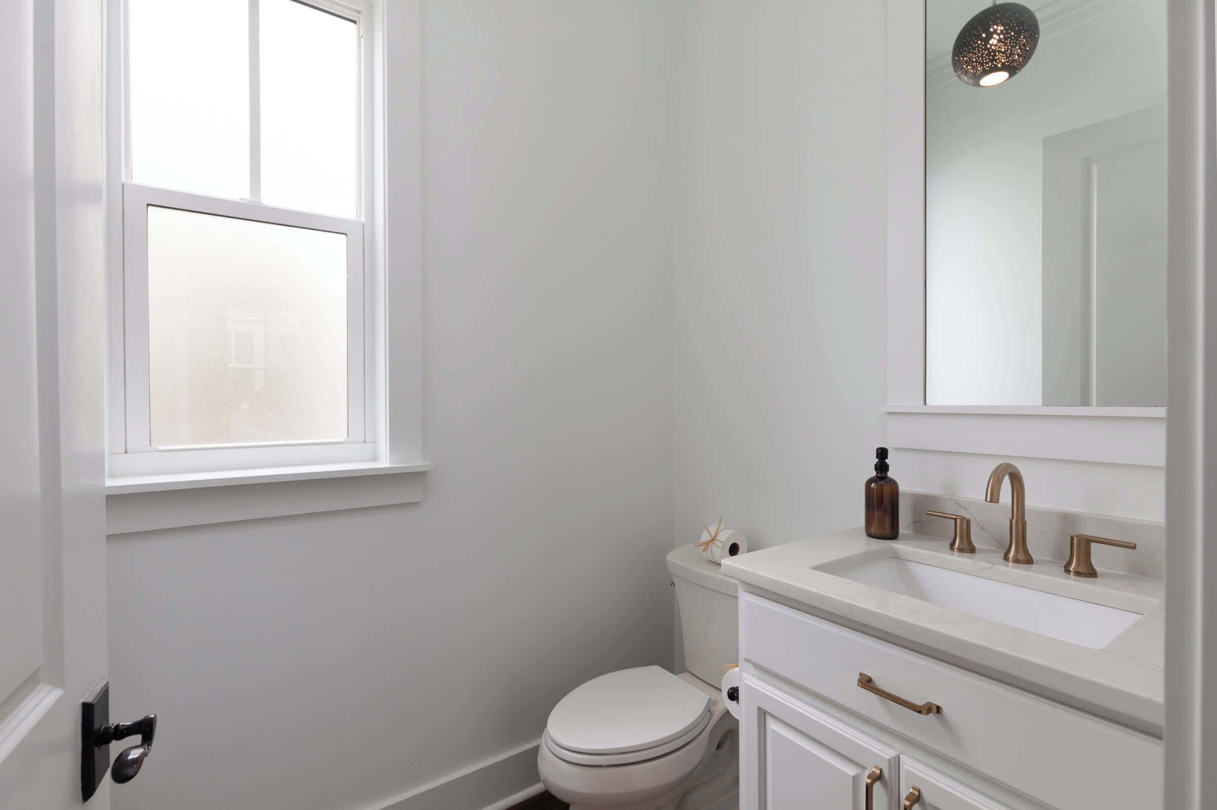 A small, white bathroom with a toilet, sink, and mirror.