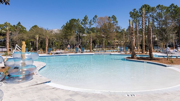 A swimming pool with clear blue water, surrounded by palm trees and lounge chairs.