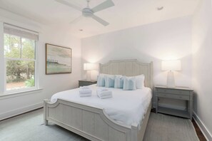 A bedroom with a bed, two bedside tables, a ceiling fan, a window, and a painting on the wall.