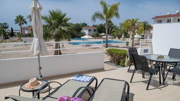 Relax on the poolside terrace with lounge chairs, a table, and umbrellas, surrounded by lush greenery and a stunning pool view.