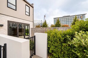Ein modernes Gebäude mit Glastür, Holzzaun und einem üppigen, grünen Heckenstreifen.