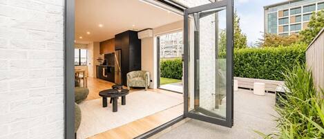 A modern house with an open sliding glass door leading to a living area with a sofa, a coffee table, and a kitchen in the background.