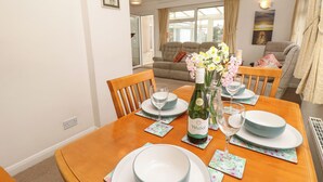 A dining table set with plates, a wine bottle, and glasses in a well-lit room with a sofa and a painting on the wall. - 14 Orchard Road (Seaview)