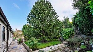 A garden with a large tree, stone pathway, and a building with a sloped roof. - Cesail Y Mynydd (Dyserth)