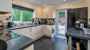A modern kitchen with white cabinets, black countertops, and a black refrigerator. - Cesail Y Mynydd (Dyserth)