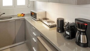 A modern kitchen with grey cabinets, a microwave, a coffee maker, and a fruit bowl on the counter. - Acropolis Hideaway Studio by GHH (Athina)