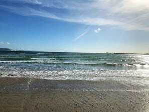 Ein Strand mit Wellen, blauem Himmel und einem entfernten Steg.