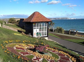 Ein kleines Holzgebäude mit einem Ziegeldach, einer Glasfront und einem Garten mit bunten Blumen davor.