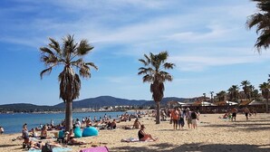 A beach with people sunbathing and swimming, palm trees, and a clear sky. - Air-conditioned apartment with sea view - Les Restanques SWIMMING POOLS TENNIS (Grimaud)