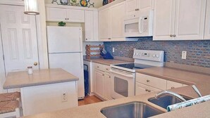Una cocina compacta con gabinetes blancos, microondas, estufa y pileta.