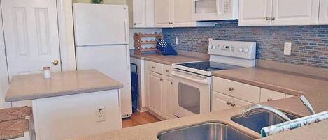 A compact kitchen with white cabinets, a microwave, a stove, and a sink.