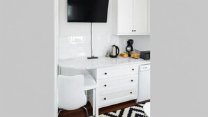 Una cocina moderna con armarios blancos, un televisor de pantalla plana montado sobre la encimera y una cafetera en la superficie.