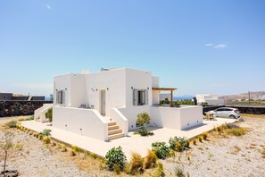 A modern white house with a patio, a car, and a view of the sea.
