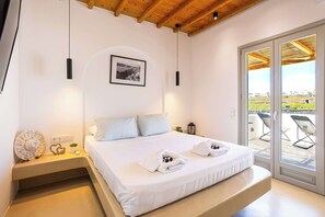 A bedroom with a bed, bedside table, lamp, picture, and a view through a sliding door to an outdoor area.