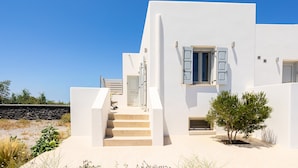 Un edificio moderno blanco con una escalera que conduce a una puerta, un pequeño árbol en primer plano y un cielo azul despejado.
