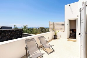 A rooftop terrace with two lounge chairs, a potted plant, and a view of the sea.