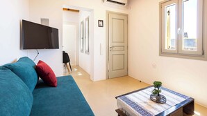 Una sala de estar con un sofá, una mesa de centro con una planta, un televisor de pantalla plana y una puerta que da a otra habitación.