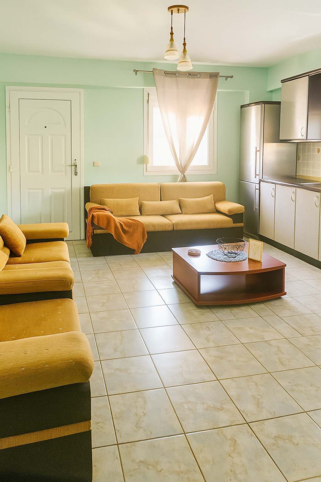 A living room with a sofa, a coffee table, and a kitchen area with a refrigerator.