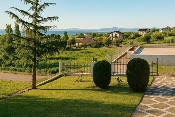 A residential area with a well-maintained lawn, a paved pathway, and a view of houses and mountains in the distance.