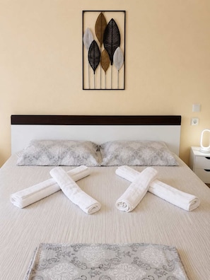 A neatly made bed with rolled towels, a patterned throw, and a wall art piece above it.