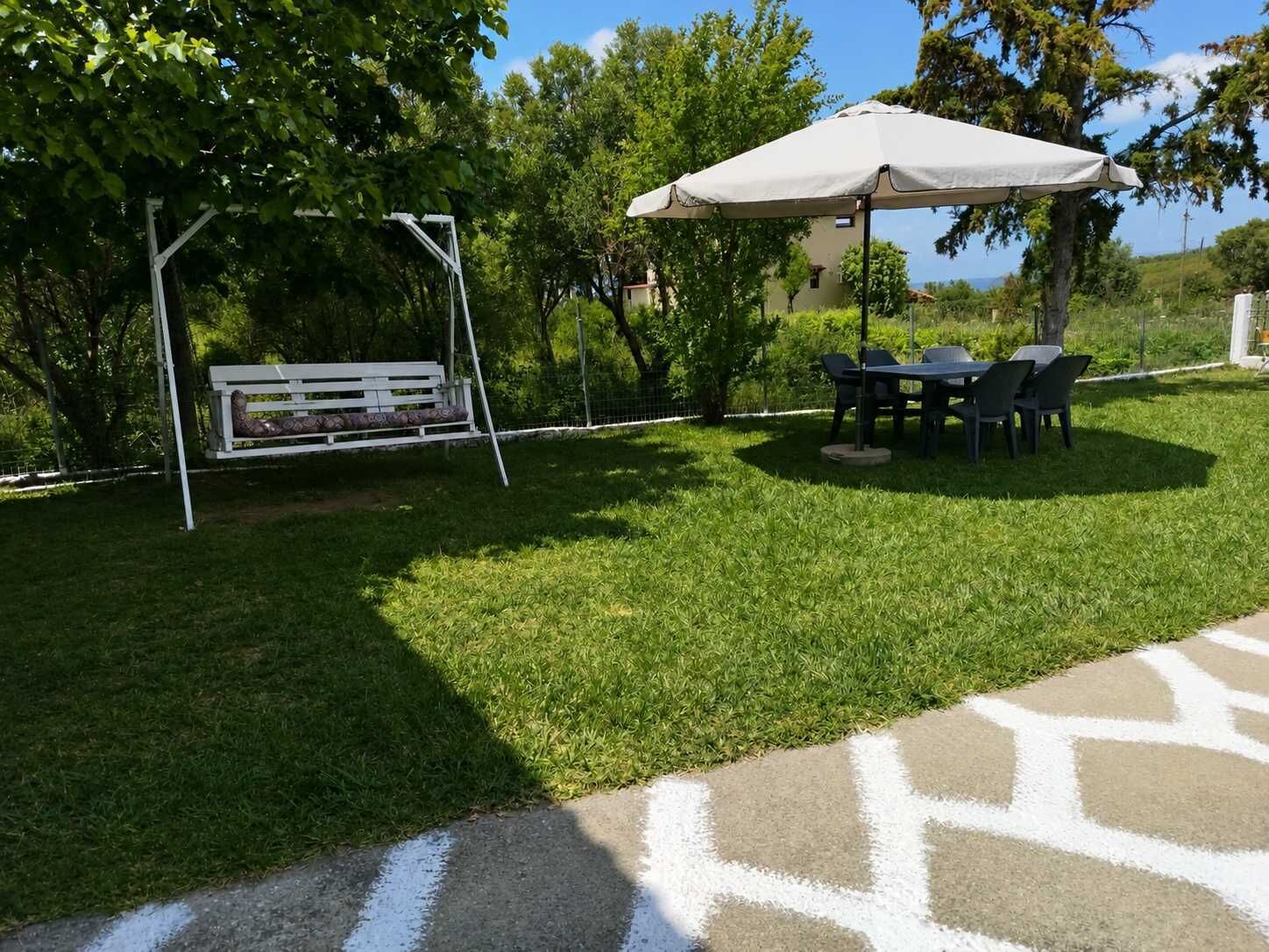 A grassy outdoor area with a swing set, a covered table and chairs, and a paved walkway.