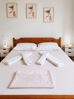 Un lit bien fait, avec du linge de lit blanc, deux tables de chevet avec des lampes et trois œuvres d’art encadrées accrochées au mur.