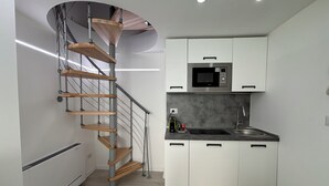 Cocina compacta con microondas integrado, lavabo y escalera de caracol.