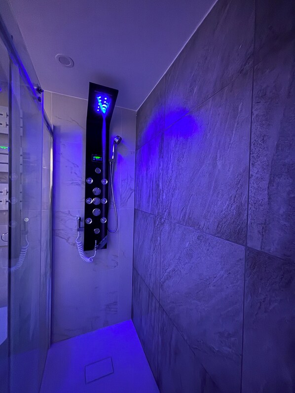 A modern shower with a control panel, a handheld showerhead, and a glass door.