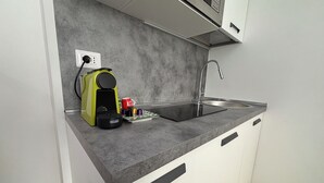 Cocina compacta con un lavamanos empotrado, una cafetera y una taza sobre la encimera.