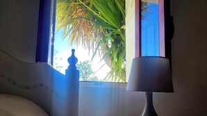 A bed with a headboard, a bedside lamp, and a window with a view of palm trees. - Casita-1 To 5guests-pool-patio-bbq-parking (Huercal-Overa)