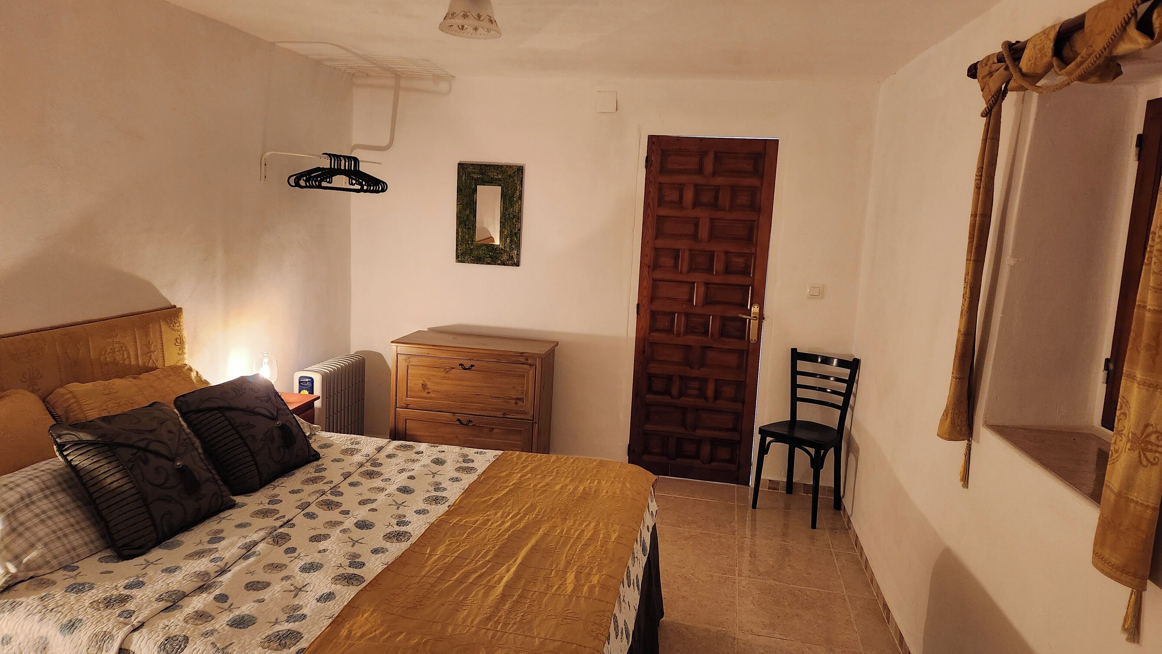 A bedroom with a bed, a wooden dresser, a chair, a radiator, and a door.
