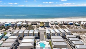 A coastal residential area with multiple two-story houses, a swimming pool, and a beach in the background. - Beach Facing, 4Bd, Sleeps 10, Bikes, BBQ, Pool (Gulf Shores)